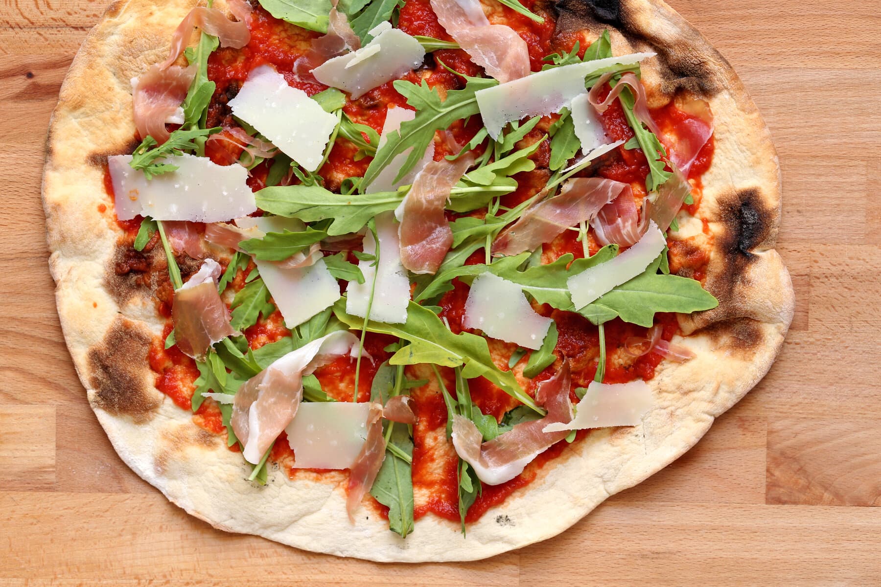 Pinsa mit Tomatensauce, Rohschinken, Rucola und Parmesan