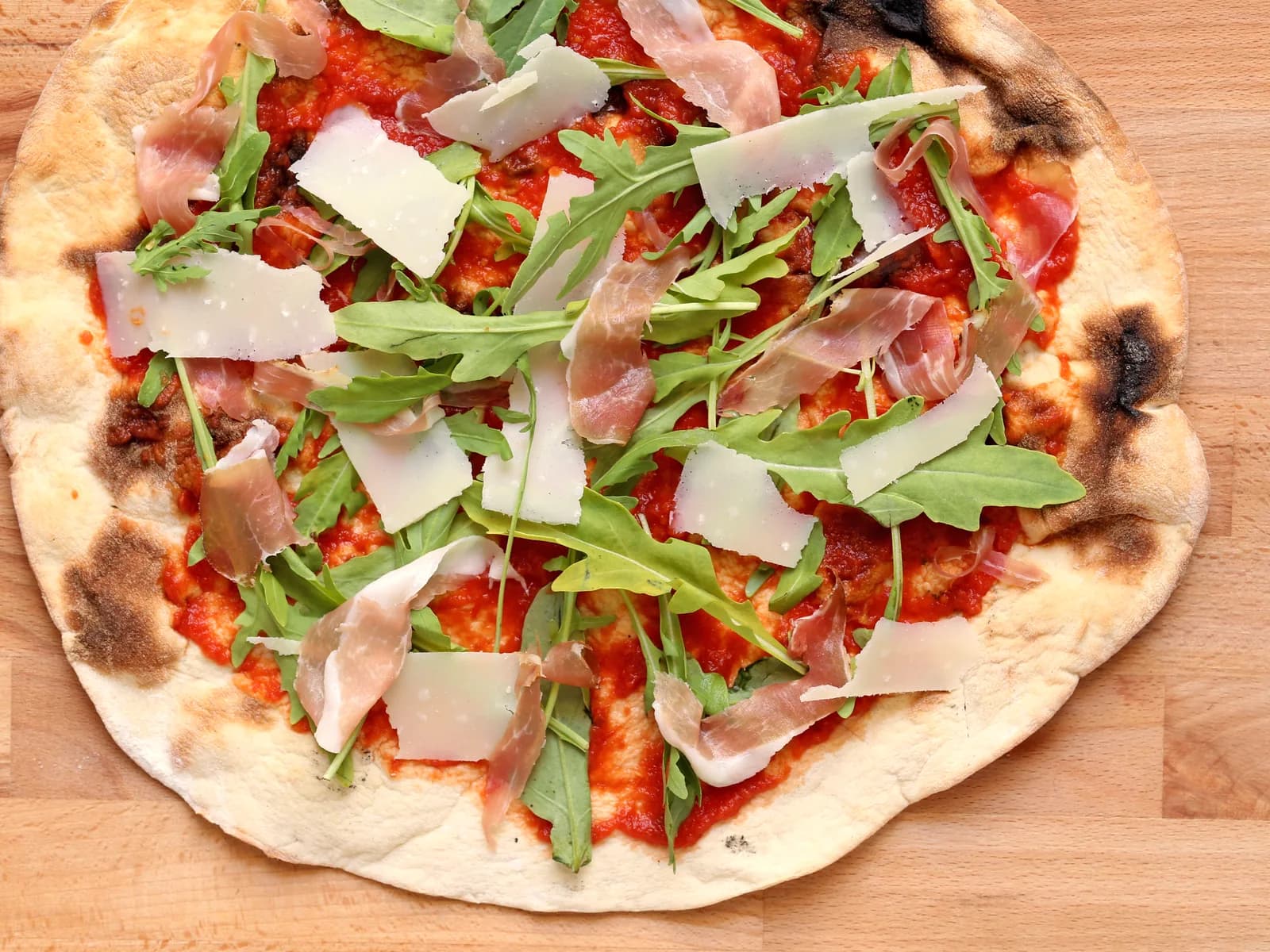 Pizza mit Tomatensauce, Rohschinken, Rucola und Parmesan